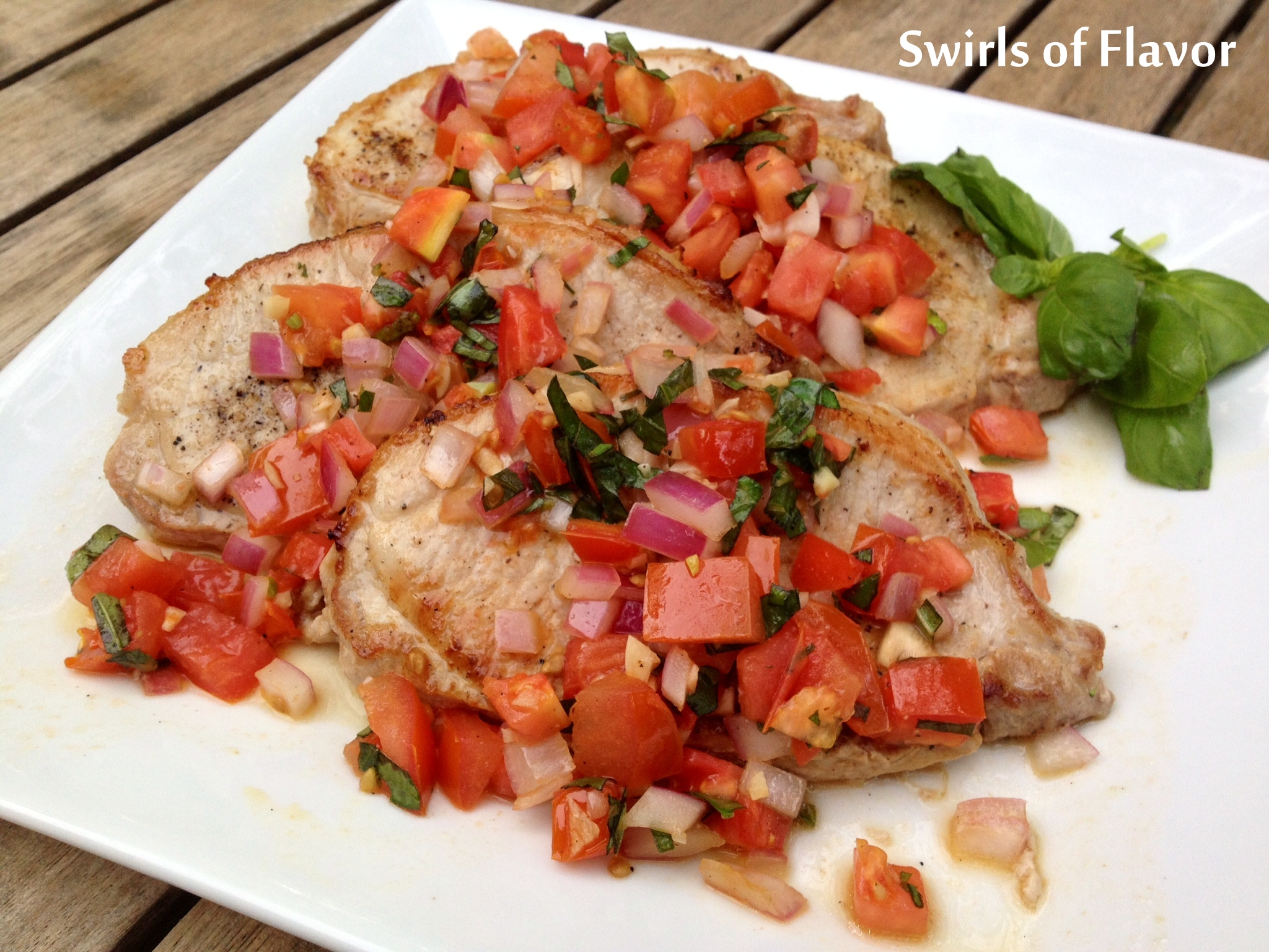 Italian pork chops with bruschetta topping and fresh basil on white plate