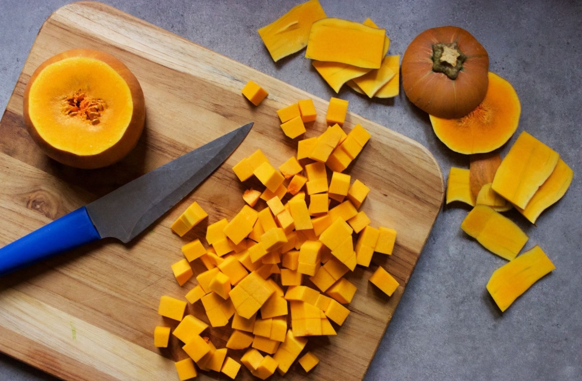 chopping butternut squash on a cutting board with a blue chef knife