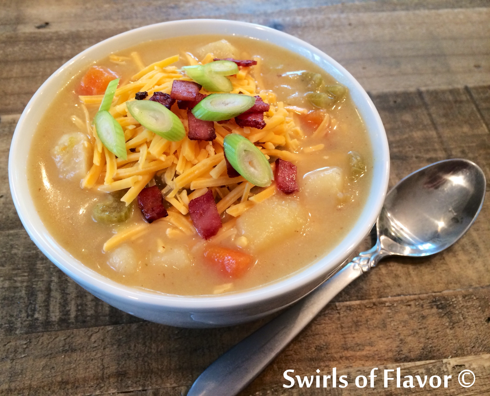 Loaded Potato Soup topped with cheese, bacon and scallions in white soup bowl