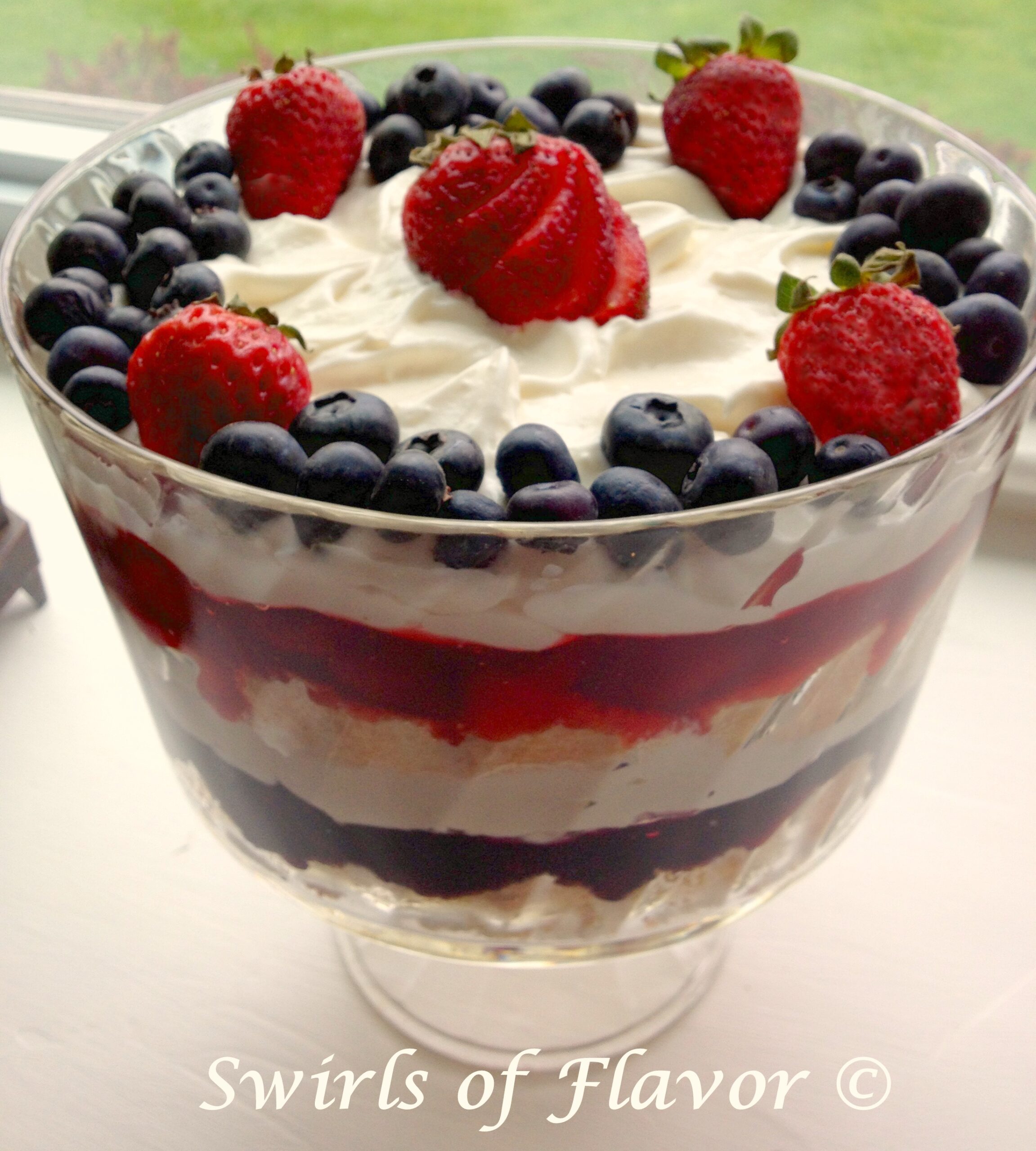 srawberries and blueberries with cake and whipped topping in a clear trifle dish