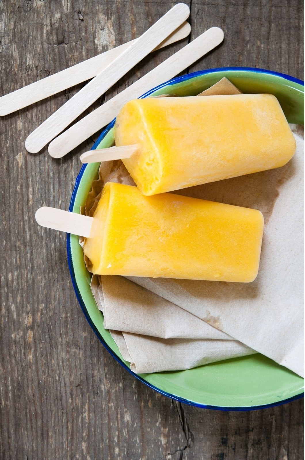 mango ice pops on a green plate wih wooden popsicle sticks