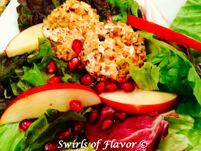 Pomegranate Apple Mixed Greens With Walnut-Crusted Goat Cheese elevates salad to a new level with homemade pomegranate vinaigrette and nutty cheese rounds! This homemade vinaigrette and easy nut crusted cheese rounds is the perfect holiday recipe! #salad #mixedgreens #homemadevinaigrette #pomegranatevinaigrette #hlidayrecipe #Thanksgiving #Christmas #tossedsalad #swirlsofflavor