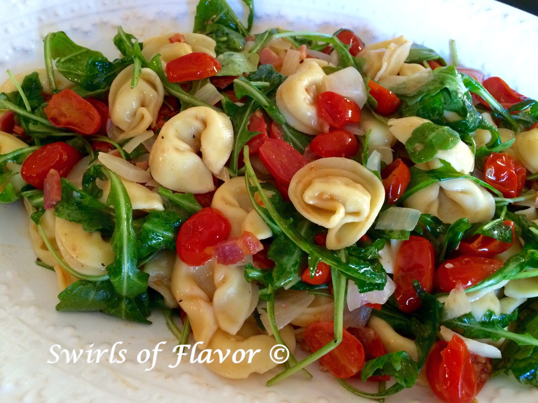 Tortellini pasta with pancetta, arugula and tomatoes on a white platter