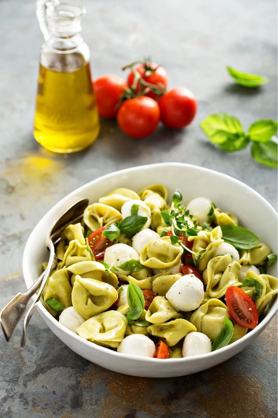pasta salad with totellini in white bol with olive oil cruet and fresh tomatoes