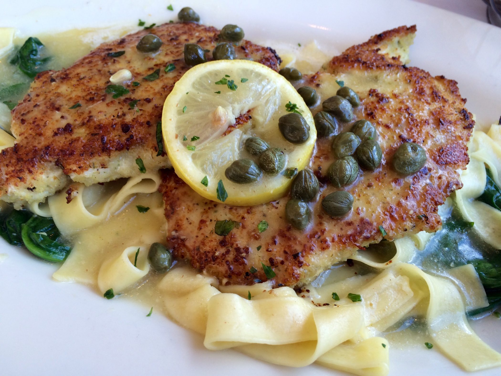 lemon caper chicken over pasta with lemon slice and capers