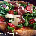 Grilled Prosciutto Parmesan & Arugula Pizza is topped with a bed of baby arugula greens lightly tossed in a white balsamic vinaigrette dressing. Baby arugula, tomatoes and prosciutto combine to make each bite the perfect combination of summer flavors.