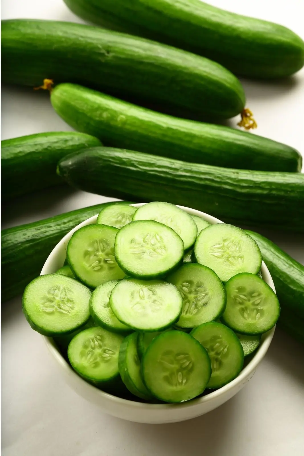 sliced cucumbers in a bowl with whole cucumbers