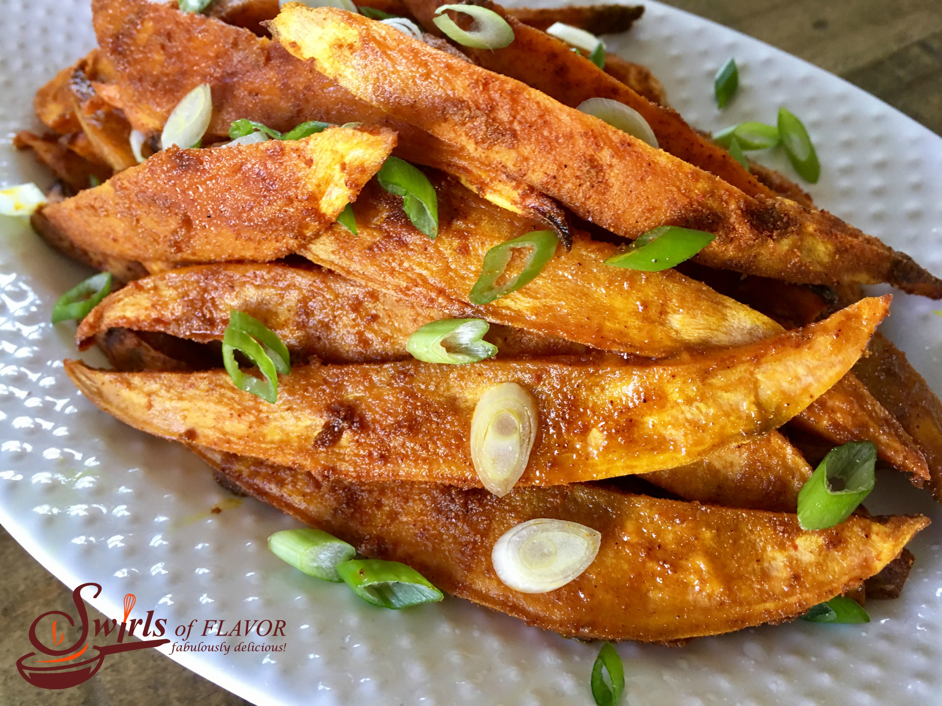 homemade sweet potato fries with sliced scallions on a white dish