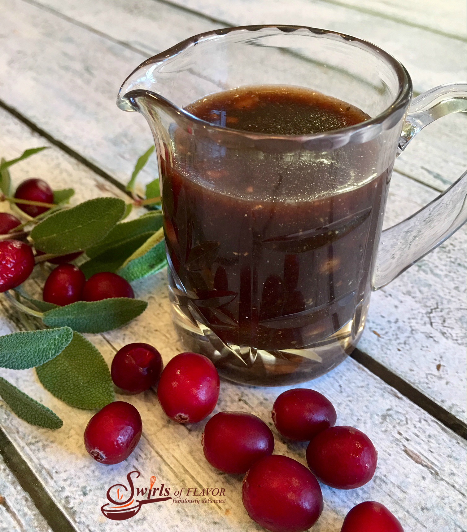 Maple Cranberry Vinaigrette in small pitcher with fresh cranberries and sage leaves