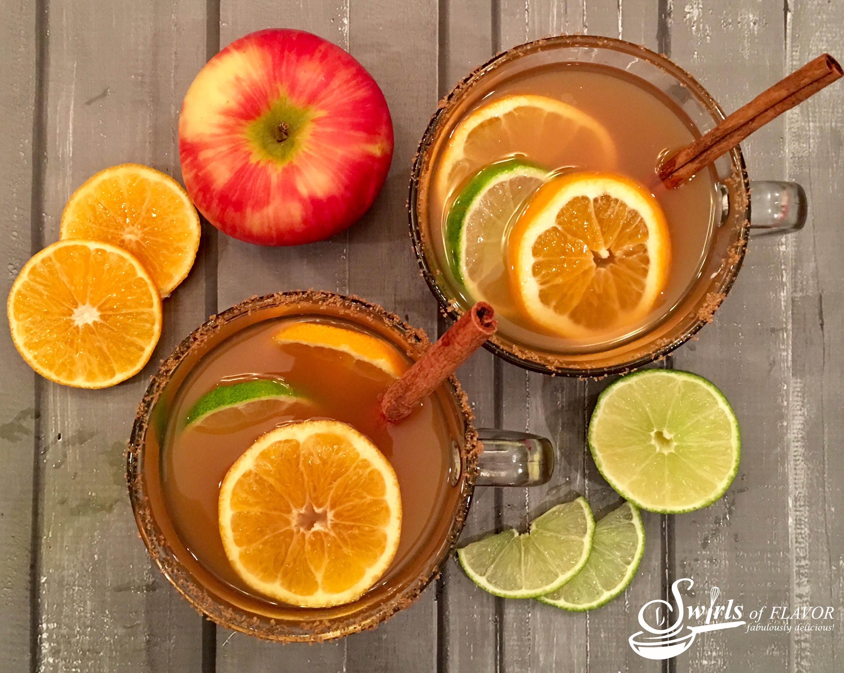 looking down on two mugs of mulled apple cider with cinnamon sticks and fresh fruit