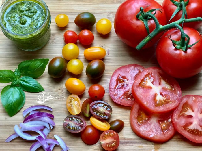 Pesto Tomato Salad is an easy 4 ingredient recipe. Garden fresh tomatoes and red onion are tossed in a homemade pesto transforming juicy tomatoes into a recipe that's bursting with fresh flavor and summertime goodness. #salad #tomato #tomatosalad #pesto #threeingredientrecipe #easyrecipe #summer #farmersmarket #heirloomtomatoes #vineripenedtomatoes #sidedish #swirlsofflavor