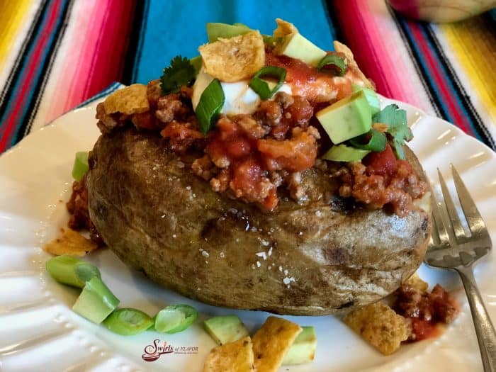 Change up Taco Tuesday with Taco Stuffed Potatoes, a twist on the traditional taco. Tender fluffy potatoes are topped with a saucy beef mixture, your favorite taco toppings and a surprise crunch of corn chips! Ready in just 25 minutes, Taco Tuesday just got a facelift! #tacotuesday #tacothursday #tacos #bakedpotatoes #tacopotatoes #groundbeef #rotel #easyrecipe #familyfavorite #stovetop #cornchips #swirlsofflavor