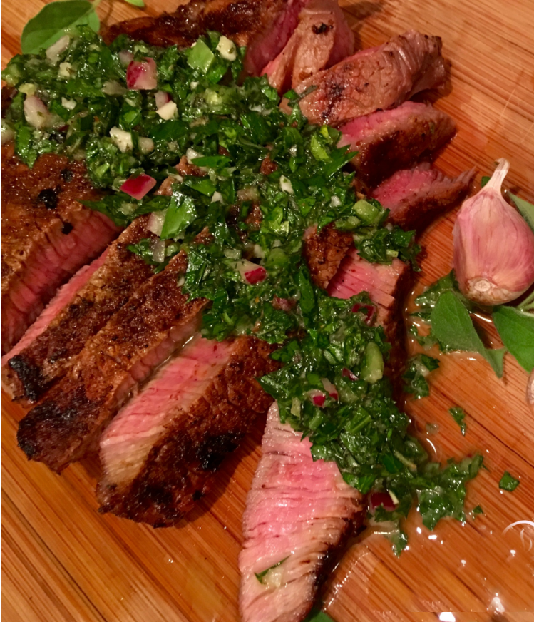 sliced steak with fresh herb sauce on wooden cutting board