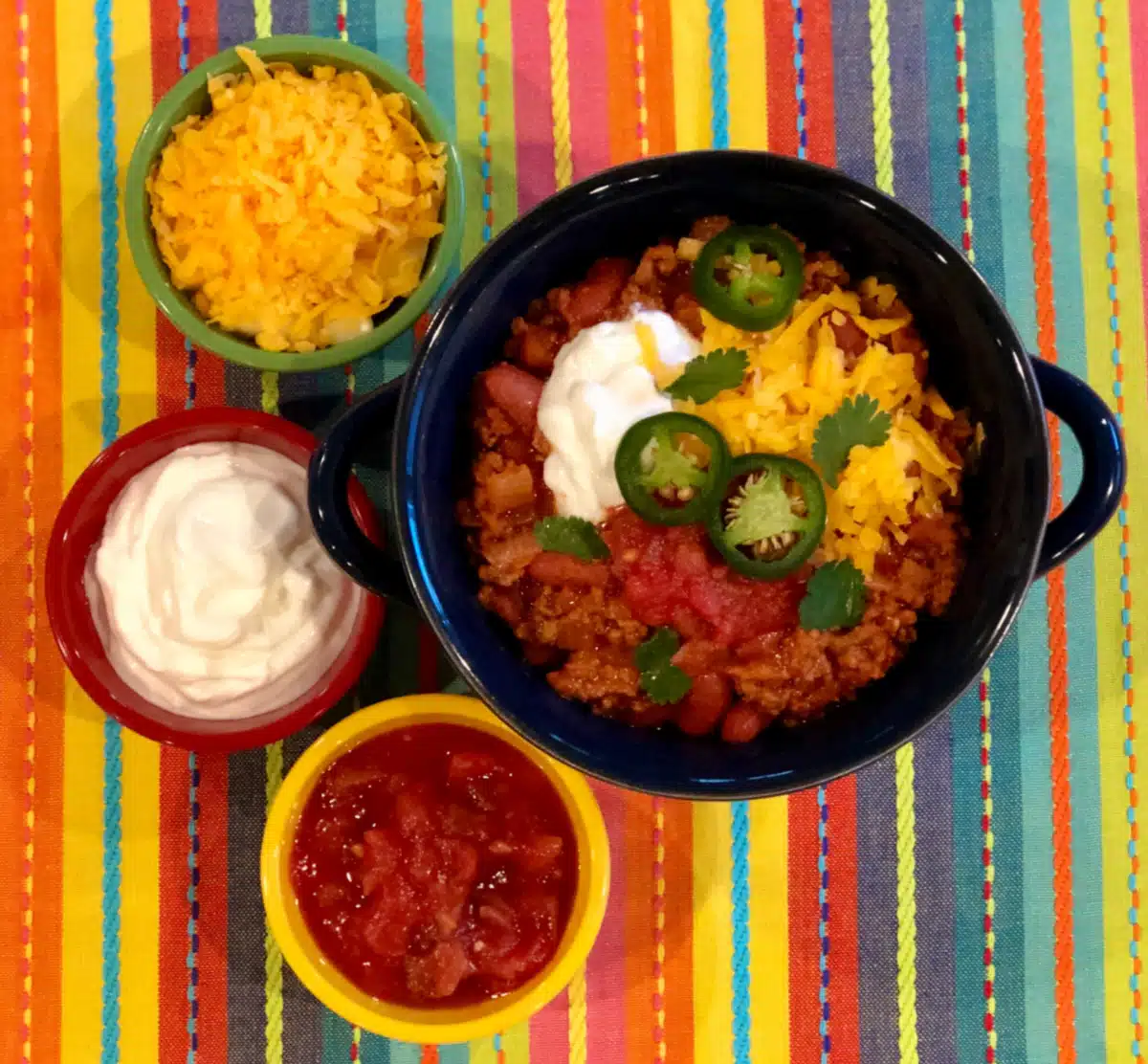 bowl of beef chili with small bowls of toppings