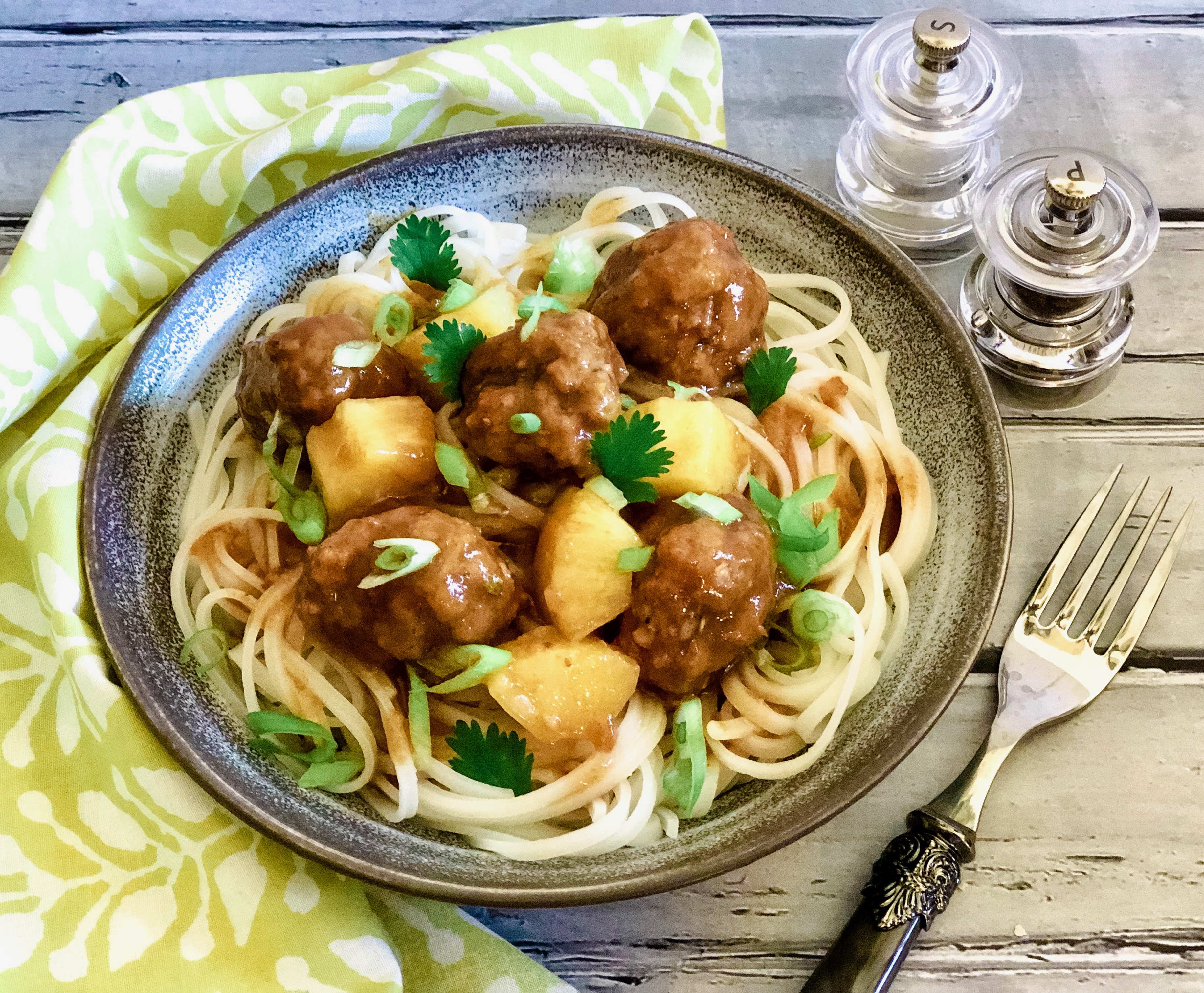 Ssweet and sour meatballs in a round dish over noodles