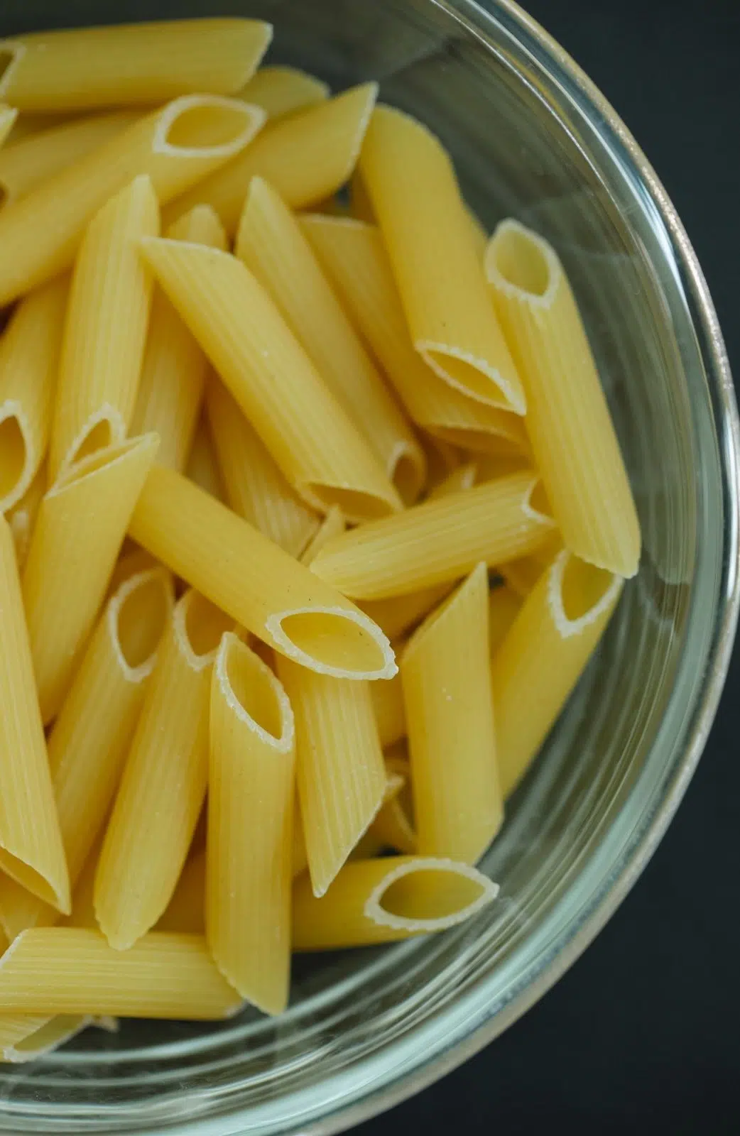 uncooked penne pasta in a clear bowl