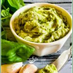 Pesto Butter in a round bowl with garlic cloves and fresh basil leaves