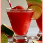 Glass of watermelon frose with straw and watermelon wedge and lime garnish