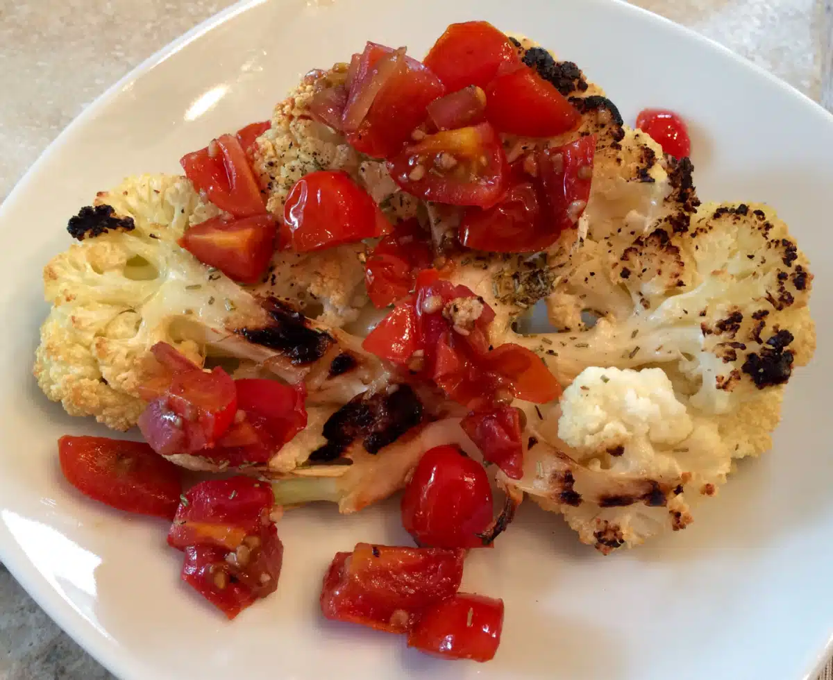 cauliflower steak with tomato topping on a white dish