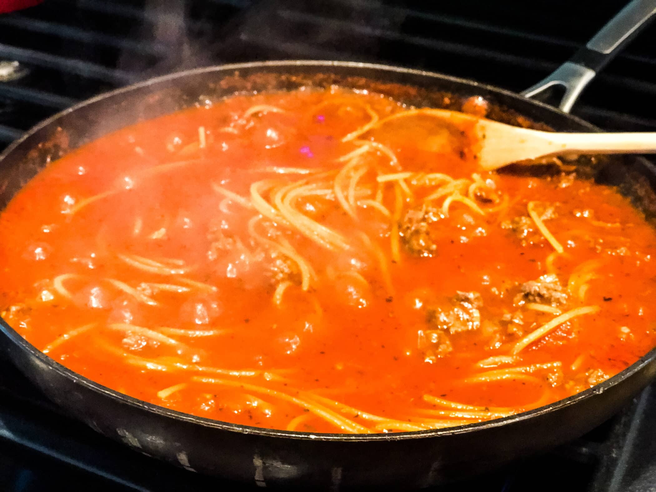 spaghetti with meat sauce cooking in a skillet