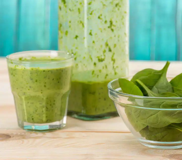 green tea smoothie in glass with bowl of baby kale