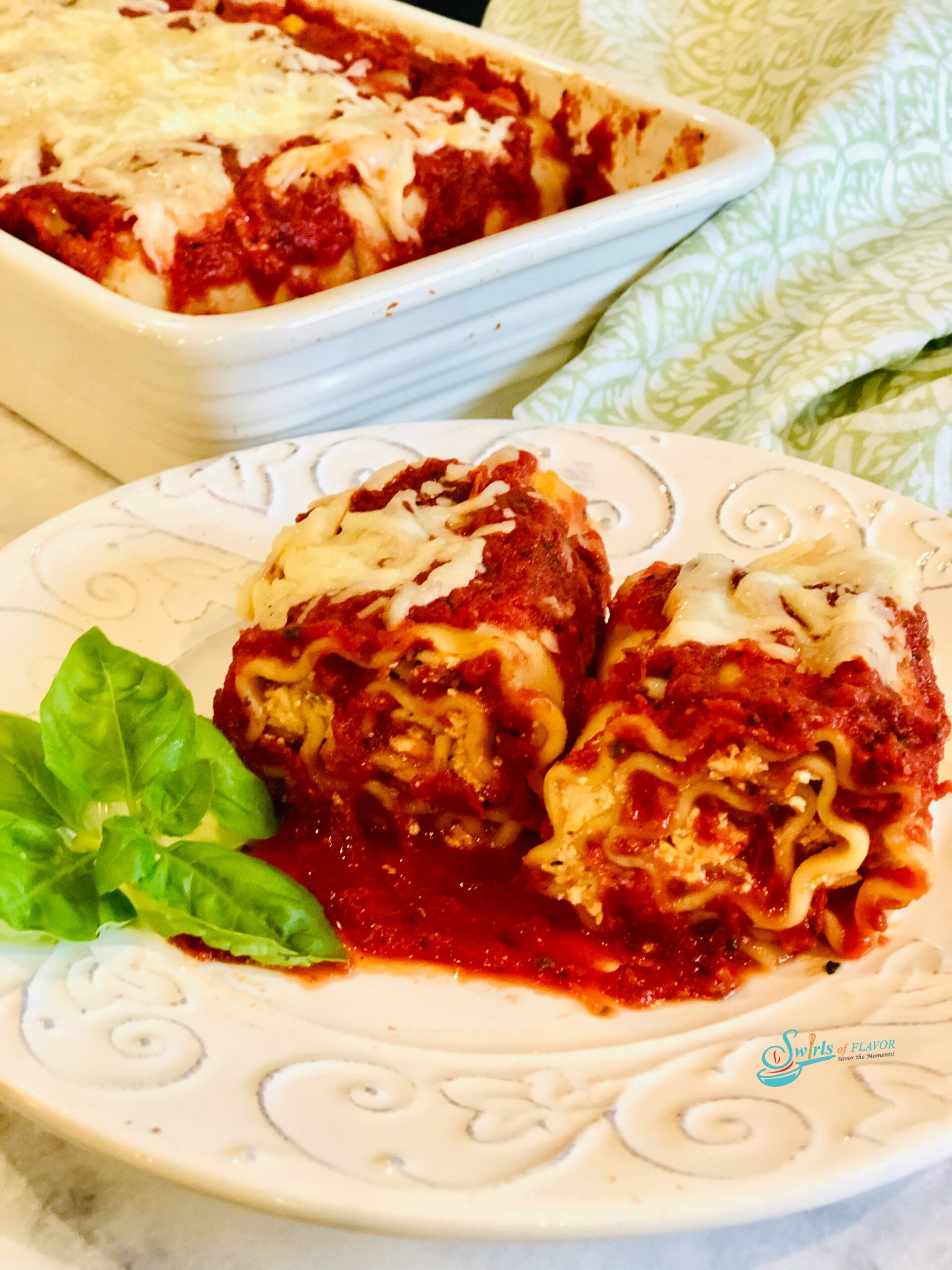 Two lasagna roll ups on a white dish with baking dish in background