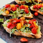 Close up photo ofBreakfast toasts with blistered tomatoes and arugula on grey slate surface