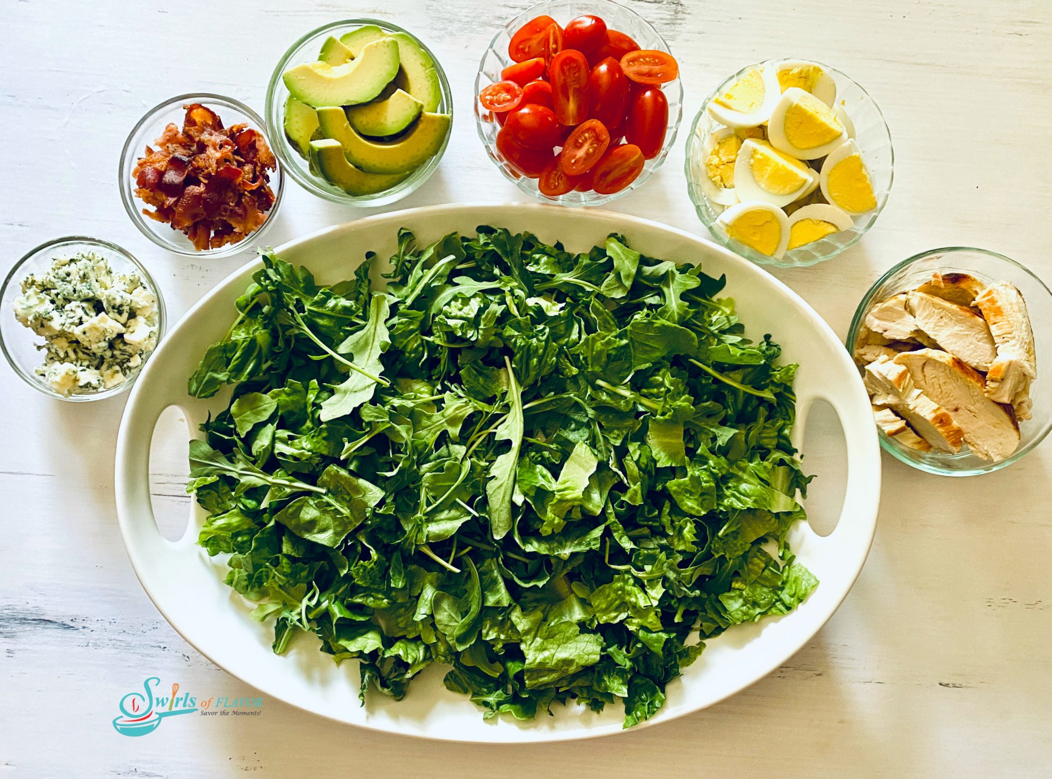 Large oval platter filled with chopped greens and small bowls of Cobb Salad ingredients