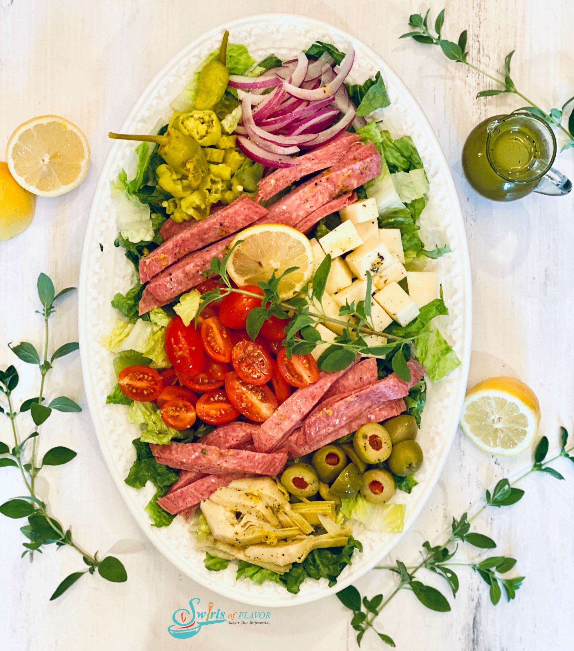 Overhead photo of Chopped Italian Salad on a white platter with fresh oregano and vinaigrette in cruet