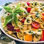 pasta salad with tomatoes and mozzarella in round bowl with fresh basil leaves and pesto