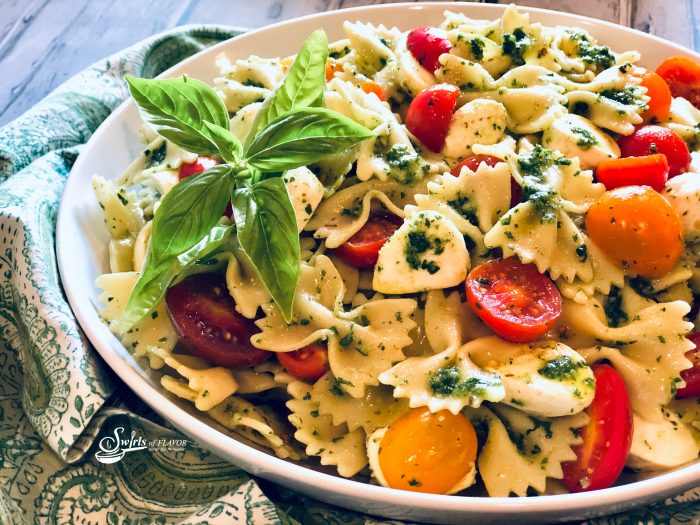 pasta salad with tomatoes and mozzarella in round bowl with fresh basil leaves and pesto