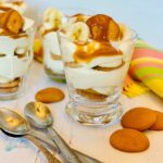 Glasses with layered banana , cookies and bananas with spoons and napkinguddin