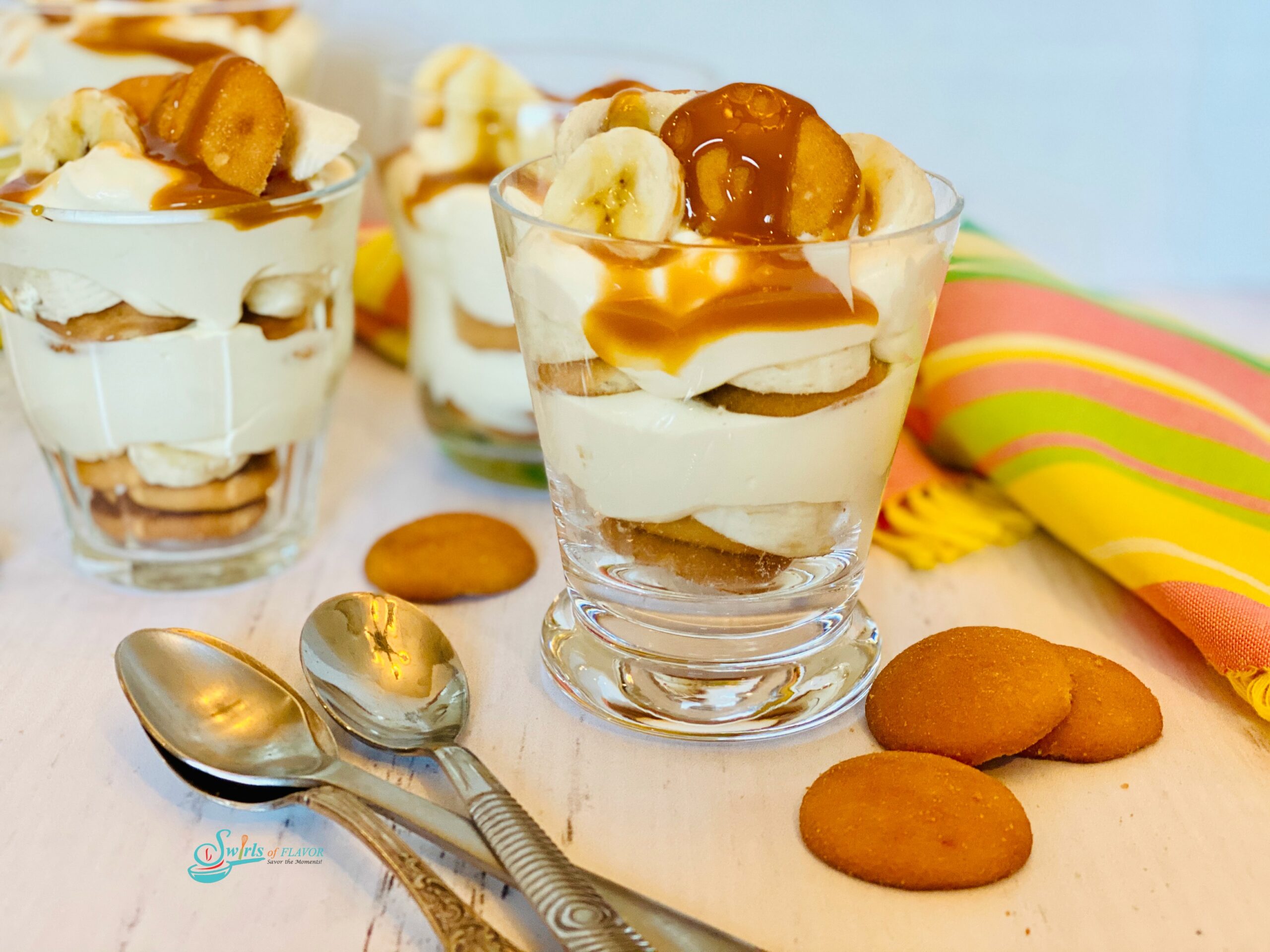 Glasses with layered banana , cookies and bananas with spoons and napkinguddin