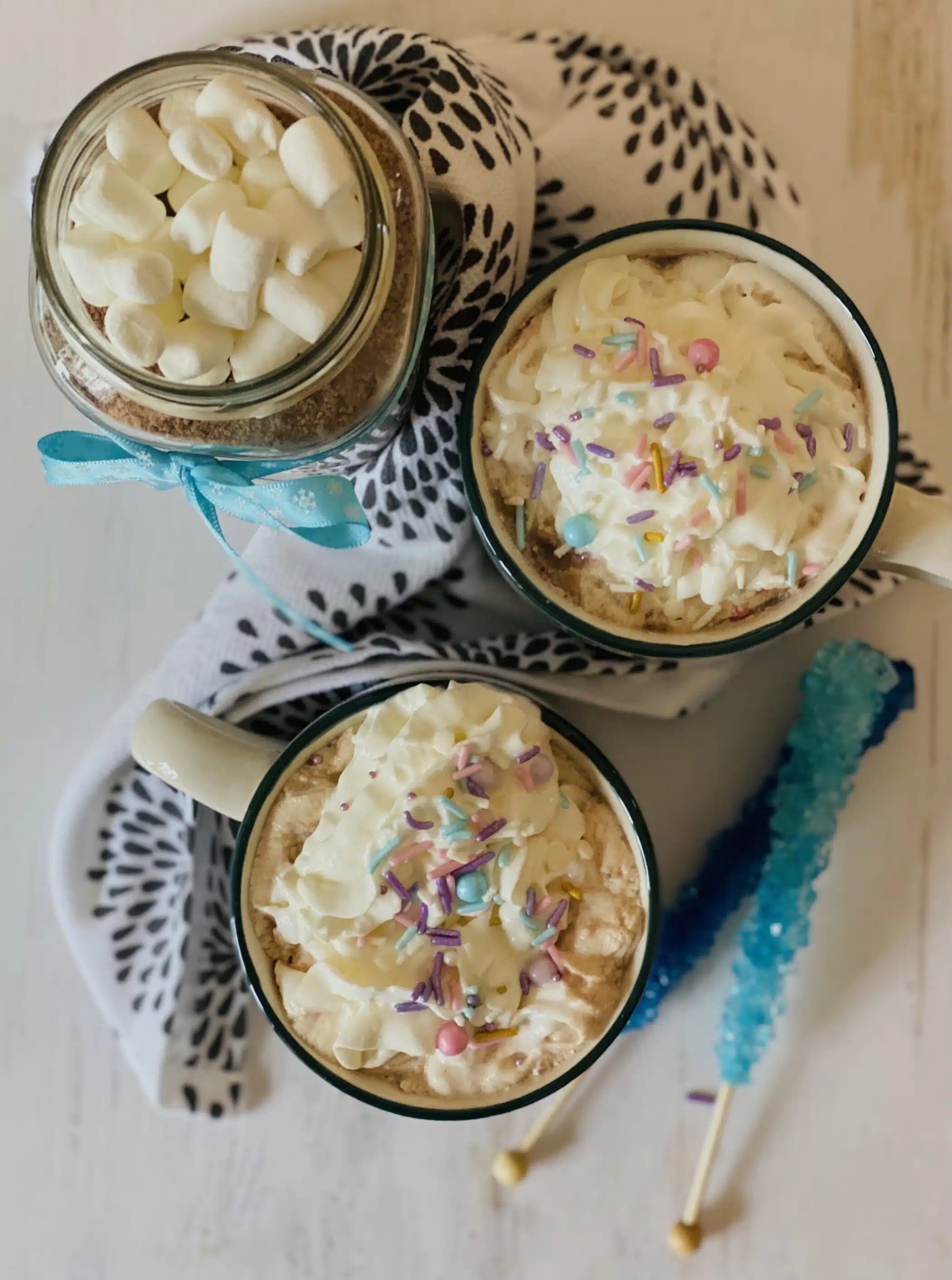 overhead of two mugs of hot chocolate with whipped cream and sprinkles