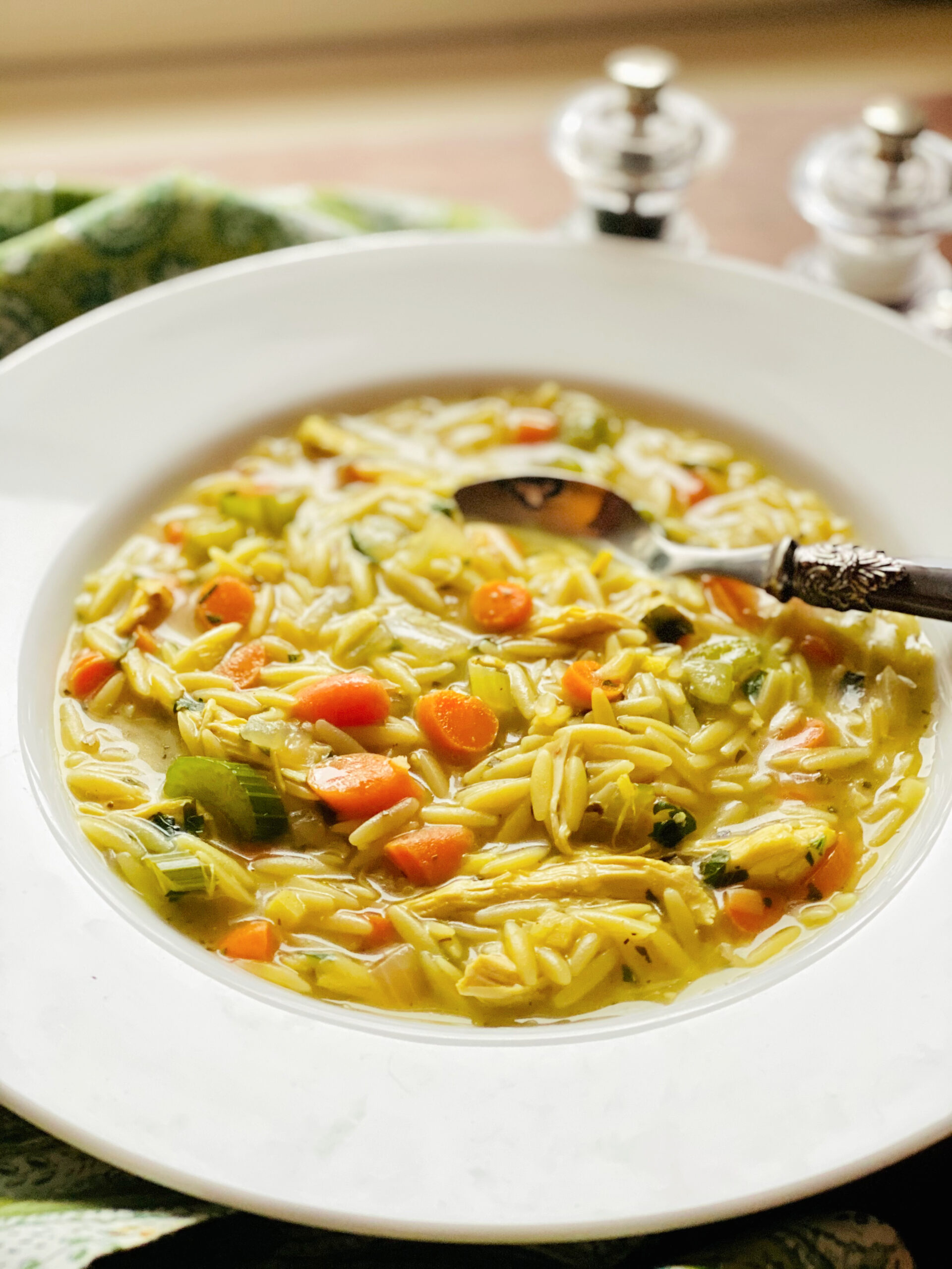 bowl of chickne orzo soup with spoon and salt and pepper shakers