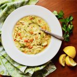 bowl of Chicken Orzo Soup with spoon, green napkin, lemon and parsley