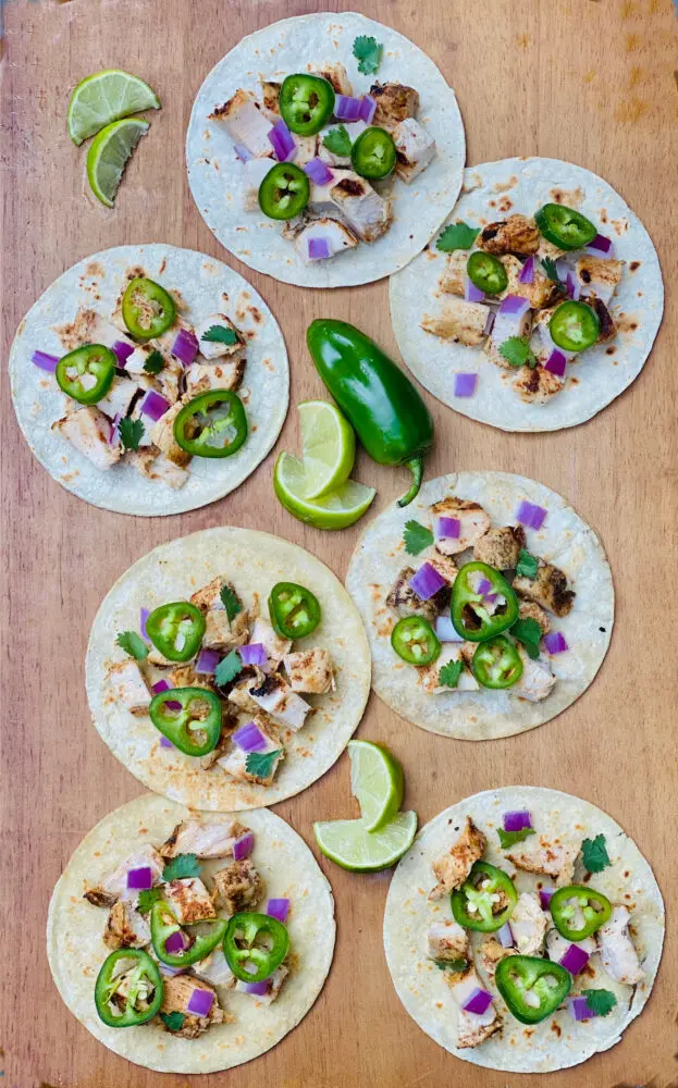 chicken street tacos on wooden board with lime wedges and jalapeno