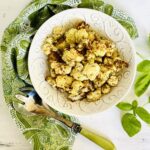 air fryer cauliflower in white bowl with green paisley napkin and fresh basil