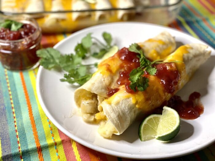 two turkey enchiladas on a plate with cilantro sprig and lime wedge