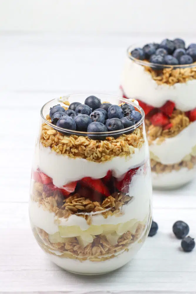 close up of two yogurt and granola parfaits with fresh fruit