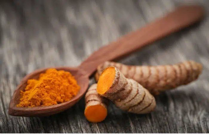 ground turmeric on a spoon and fresh turmeric