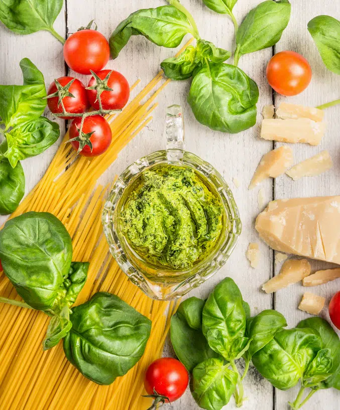 pesto in a jar with fresh basil leaves and tomatoes