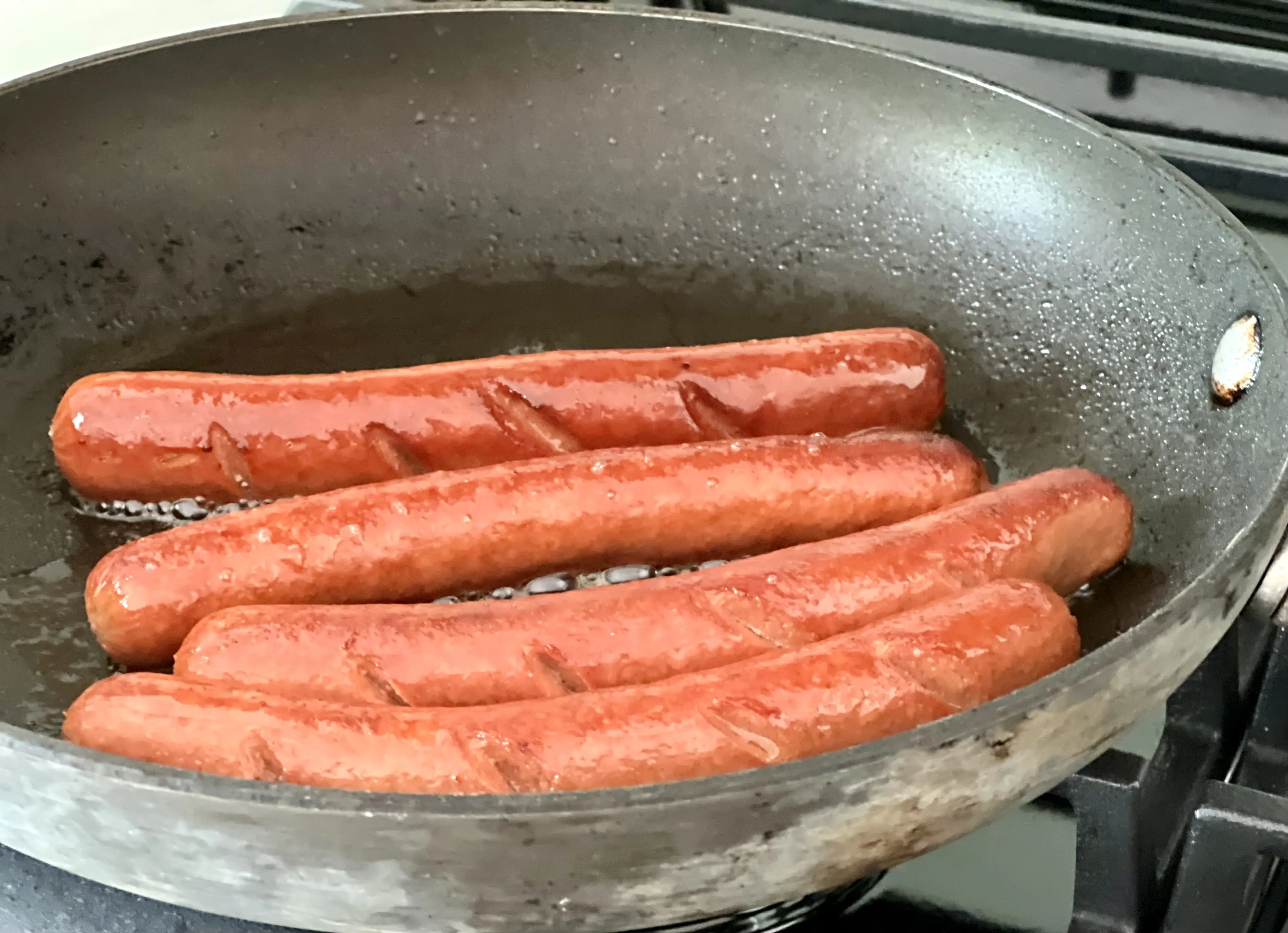 hot dogs cooking in a skillet