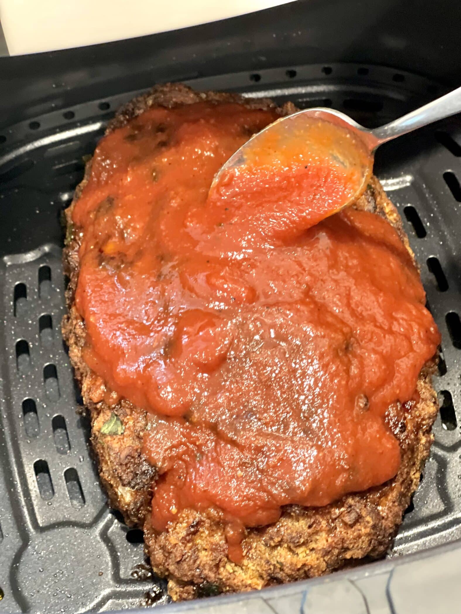 spooning barbecue sauce over meatloaf in the air fryer