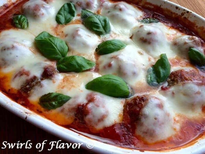 meatballs parmesan in a baking dish topped with fresh basil leaves