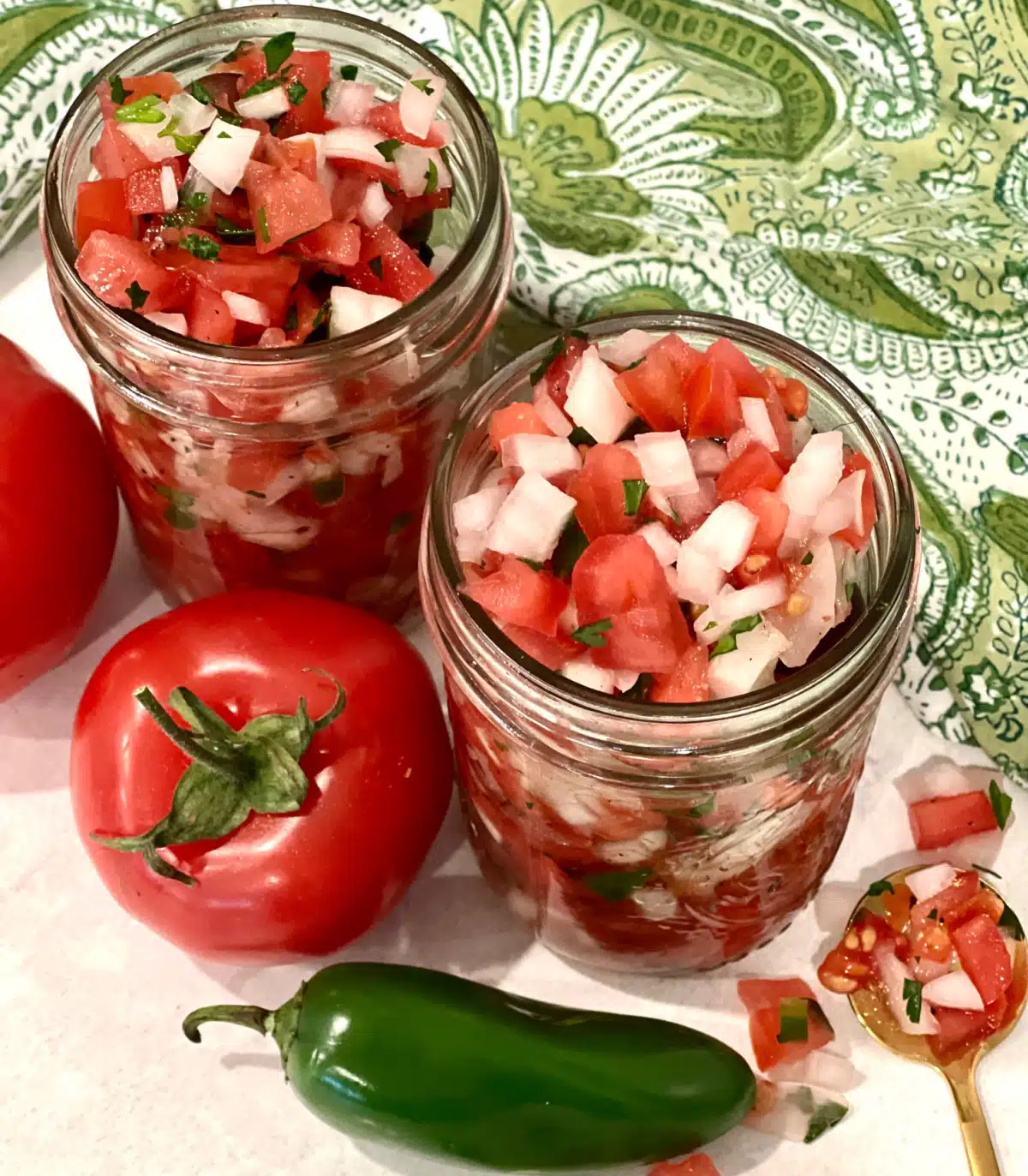 overhead of tomato relish in mason jars with tomato, jalapeno and green print napkin
