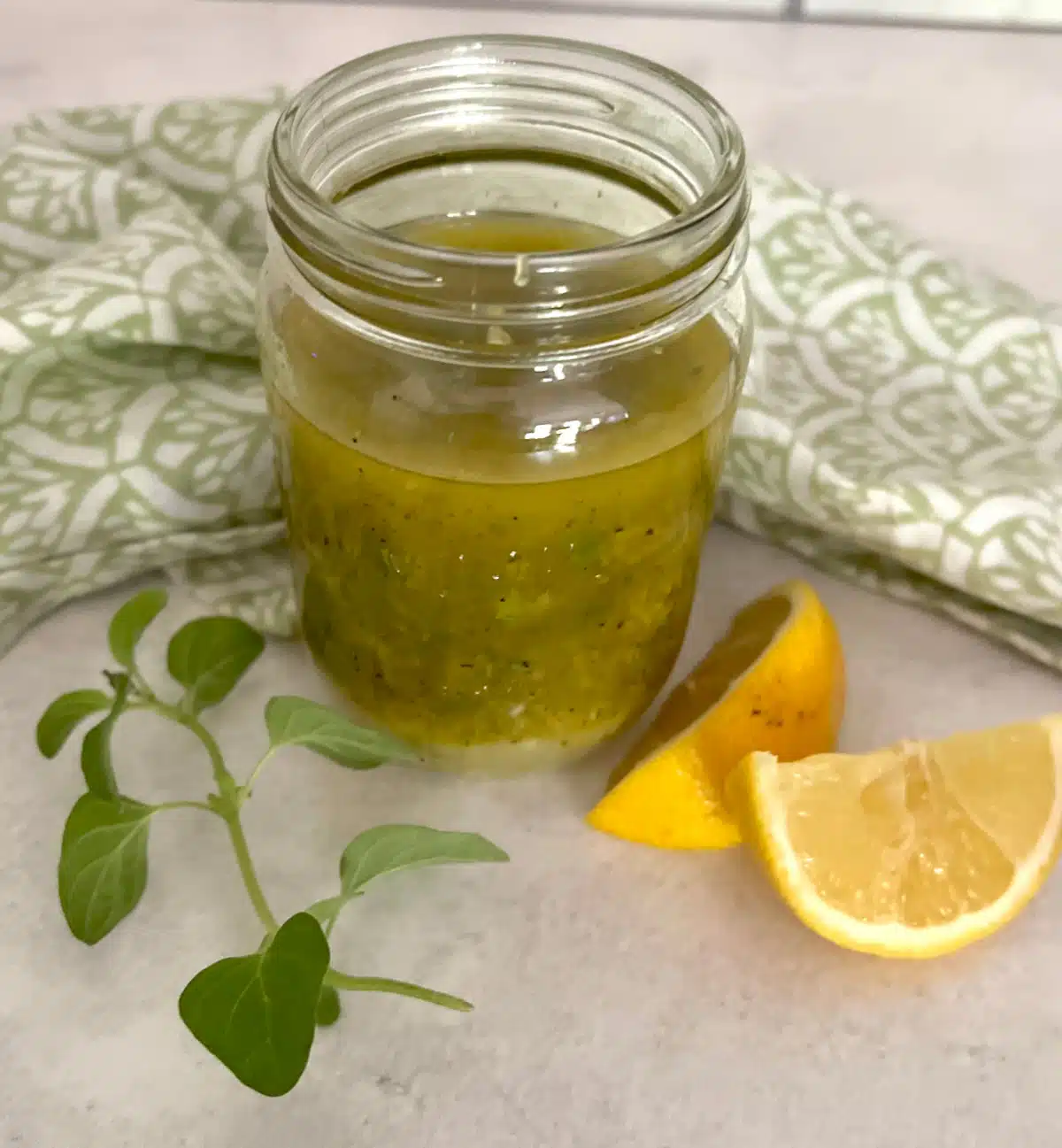 greek salad dressing in a jar with lemon wedges and fresh oregano