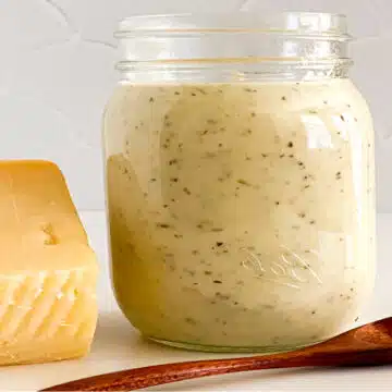 jar of garlic parmesan sauce with wedge of cheese and wooen spoon