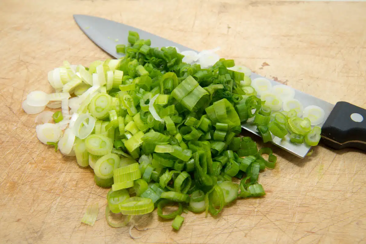 chopped scallions on a wooden board with chef knife