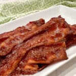 bacon cooked in the oven on a white platter with a green print napkin
